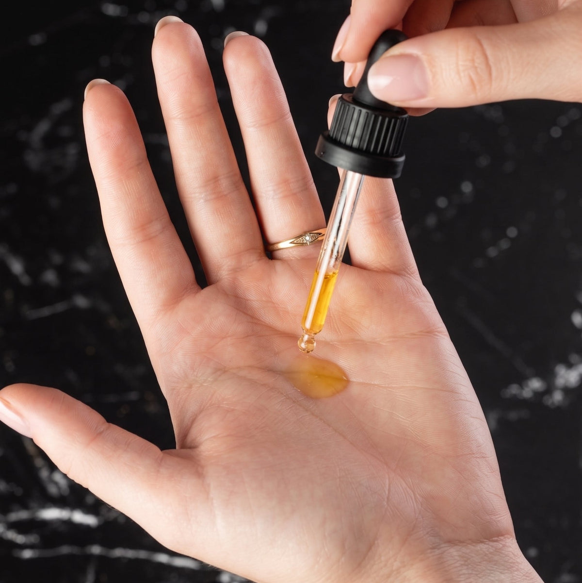 A close-up of a hand holding a dropper above another open palm, with golden serum being dispensed into the skin. A small bottle labeled VALERI SKIN is visible at the bottom, set against a dark marble background.